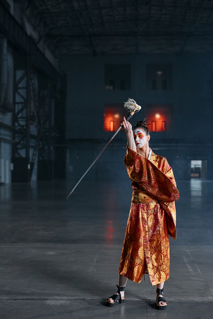 A cosplayer in traditional geisha attire showcases a dramatic pose with a sword in a dim warehouse.